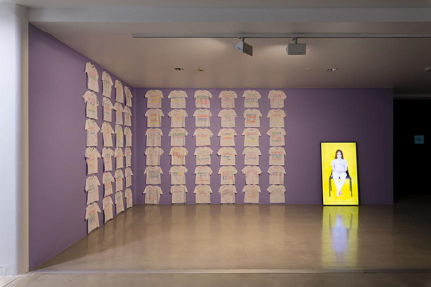 Installation view of LARA THOMS’s (left) Blatantly Disrespectful, 2019, cotton t-shirts and puff paint, dimensions variable; and (right) Heading Down the Wrong Path, 2019, single-channel video with color, no sound: 2 min 11 sec, at “OK Democracy, We Need to Talk,” Campbelltown Arts Centre, Sydney, 2019.